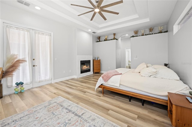 bedroom with ceiling fan, a tray ceiling, and light hardwood / wood-style flooring