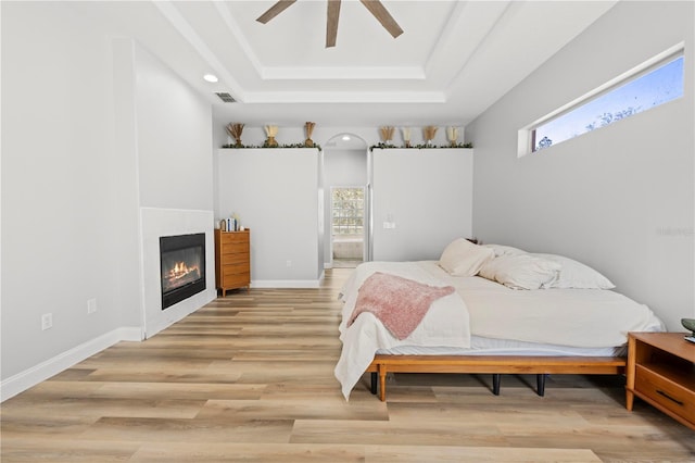 bedroom featuring ceiling fan, light hardwood / wood-style floors, a tray ceiling, and multiple windows