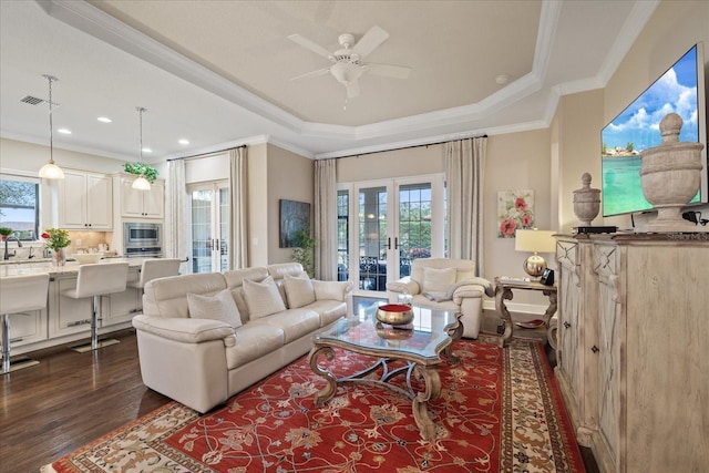 living room featuring ceiling fan, dark hardwood / wood-style flooring, french doors, ornamental molding, and a tray ceiling