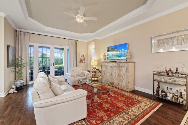 living room featuring a raised ceiling, ceiling fan, ornamental molding, and dark wood-type flooring