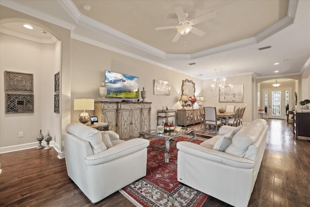 living room featuring ceiling fan with notable chandelier, dark wood-type flooring, a raised ceiling, and ornamental molding