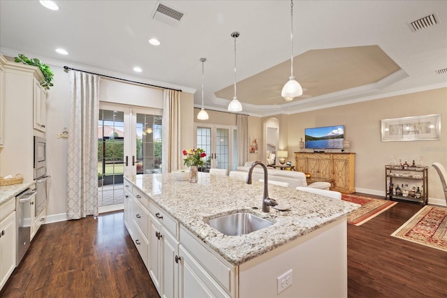 kitchen with french doors, a kitchen island with sink, a tray ceiling, and sink