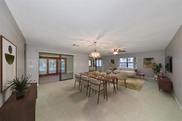 carpeted dining space with ceiling fan with notable chandelier and a textured ceiling