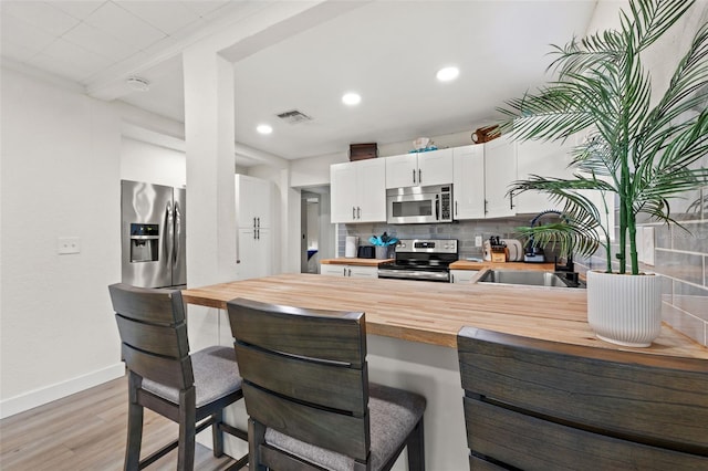 kitchen featuring a kitchen bar, wooden counters, appliances with stainless steel finishes, white cabinets, and sink