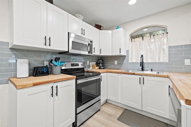 kitchen with wooden counters, white cabinetry, stainless steel appliances, sink, and light wood-type flooring