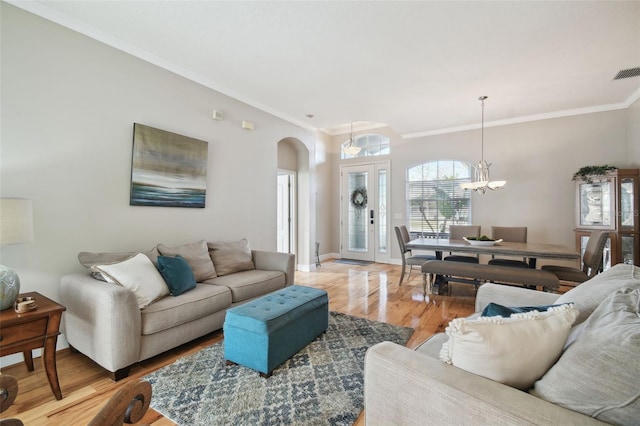 living room with light wood-type flooring, crown molding, and a chandelier