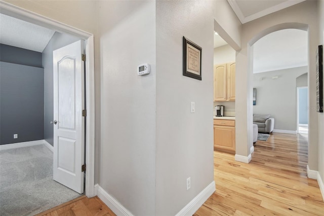 hallway with light wood-type flooring and crown molding