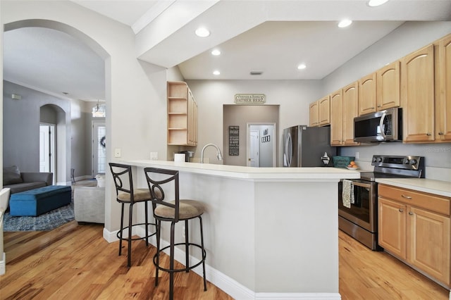 kitchen with kitchen peninsula, light brown cabinetry, light hardwood / wood-style floors, a kitchen bar, and appliances with stainless steel finishes