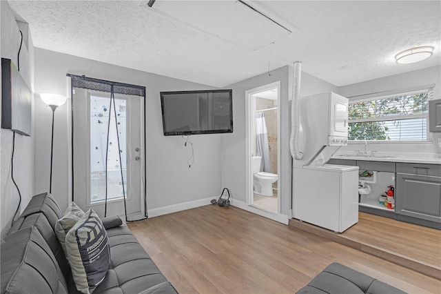 living room featuring stacked washer and dryer, a wealth of natural light, light hardwood / wood-style floors, and sink