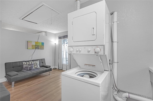 laundry room with stacked washer / drying machine, a textured ceiling, and light hardwood / wood-style flooring