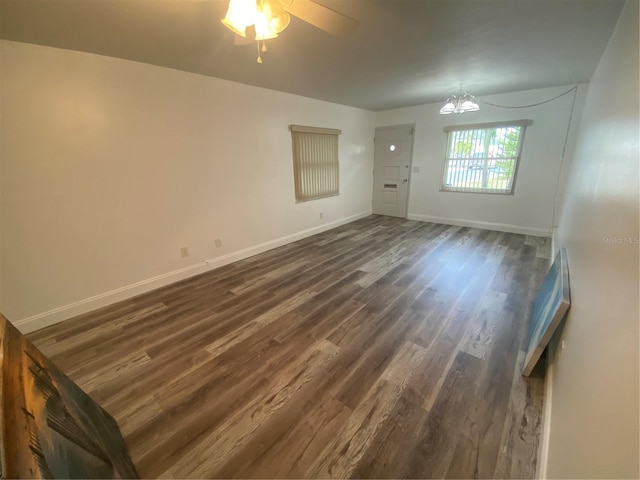 spare room with ceiling fan with notable chandelier and dark wood-type flooring