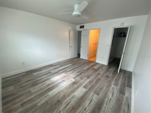 unfurnished bedroom with dark wood-type flooring, connected bathroom, a walk in closet, a closet, and ceiling fan