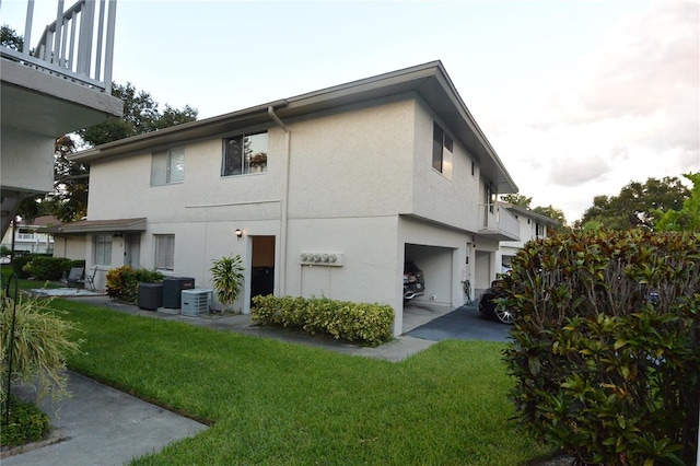 view of side of property featuring a garage, a lawn, a balcony, and central AC