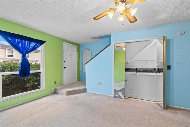 unfurnished living room featuring a textured ceiling, washing machine and dryer, ceiling fan, and light colored carpet