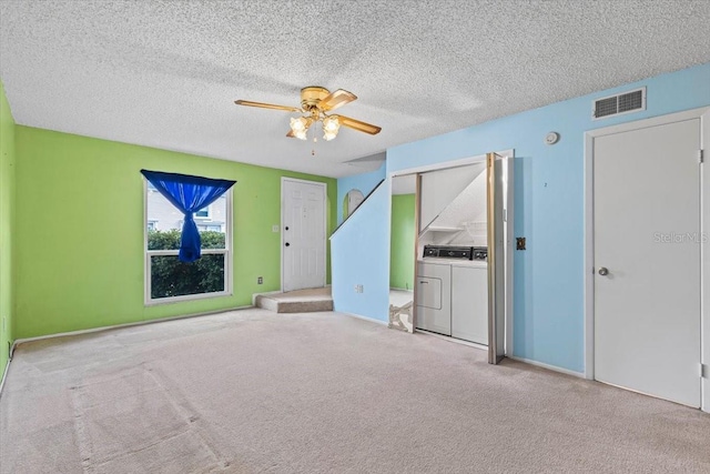 interior space featuring a textured ceiling, ceiling fan, separate washer and dryer, and light carpet