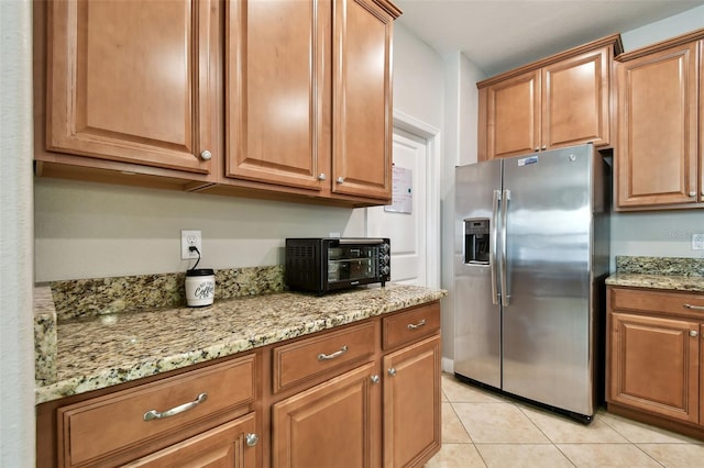 kitchen featuring light tile patterned flooring, stainless steel fridge, and light stone counters