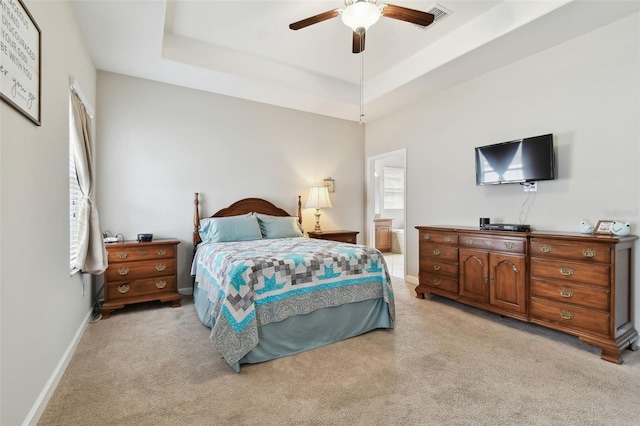 bedroom featuring ceiling fan, ensuite bathroom, a raised ceiling, and light carpet