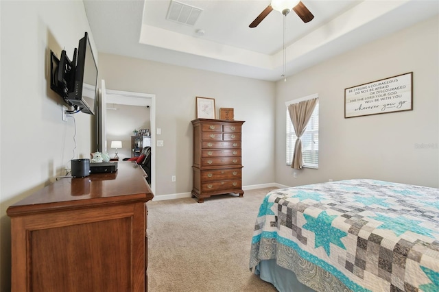 bedroom with ceiling fan, light colored carpet, and a tray ceiling