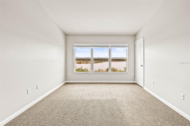 spare room featuring light colored carpet, a textured ceiling, and a water view