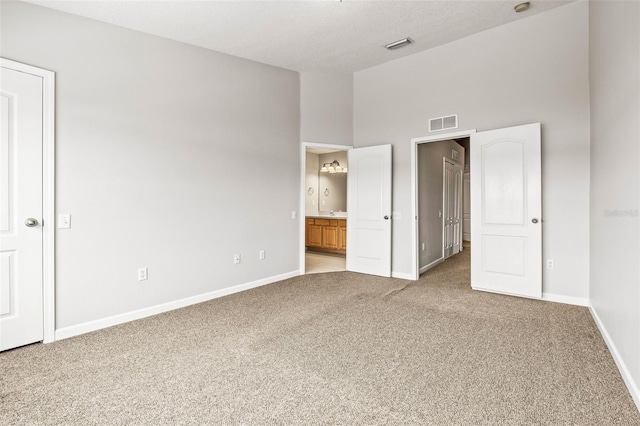 unfurnished bedroom with a high ceiling, connected bathroom, and light colored carpet