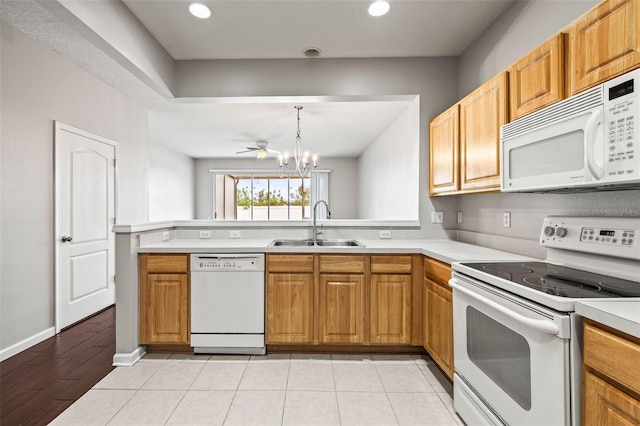 kitchen featuring sink, decorative light fixtures, kitchen peninsula, white appliances, and ceiling fan with notable chandelier