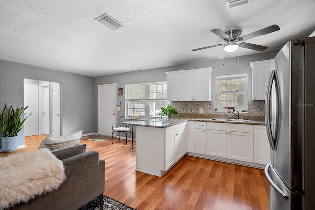 kitchen with white cabinetry, stainless steel fridge, dark stone countertops, wood-type flooring, and sink