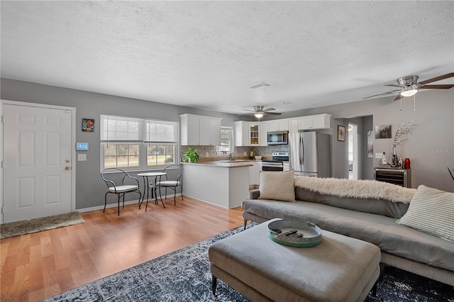 living room with ceiling fan, light wood-type flooring, sink, and a textured ceiling