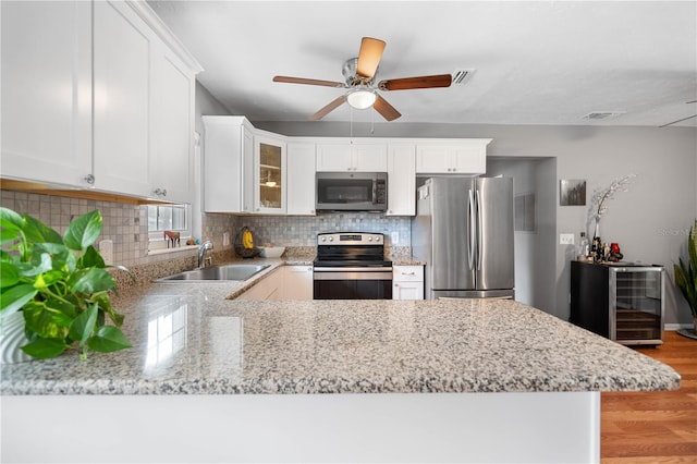 kitchen with white cabinetry, kitchen peninsula, appliances with stainless steel finishes, decorative backsplash, and sink