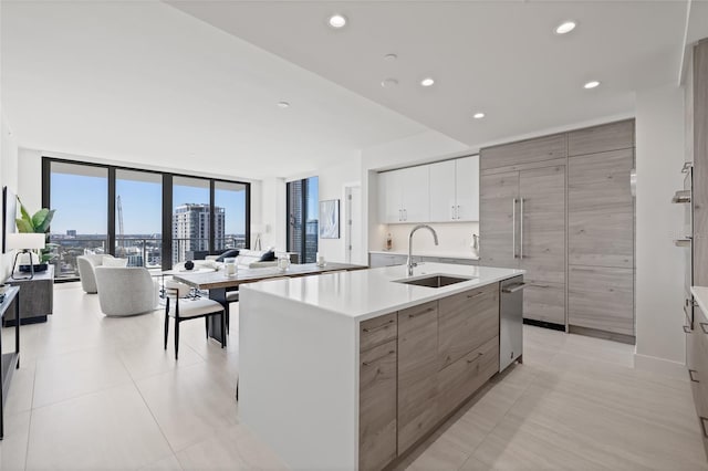 kitchen featuring floor to ceiling windows, sink, white cabinetry, stainless steel dishwasher, and an island with sink