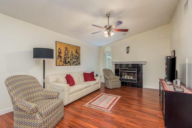 living room featuring dark wood-type flooring, a textured ceiling, lofted ceiling, a tiled fireplace, and ceiling fan