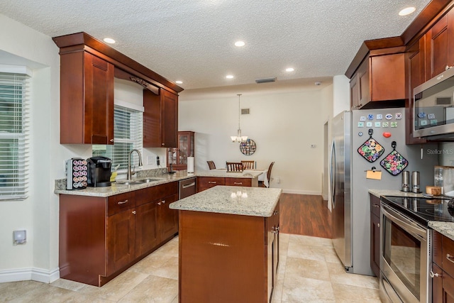 kitchen featuring appliances with stainless steel finishes, hanging light fixtures, light stone countertops, a kitchen island, and sink