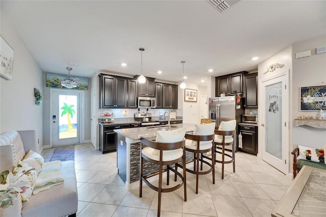 kitchen with tasteful backsplash, stainless steel appliances, a kitchen island with sink, and pendant lighting