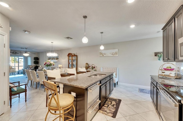 kitchen featuring a kitchen island with sink, stainless steel appliances, light stone countertops, dark brown cabinetry, and sink