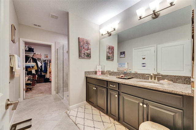 bathroom with a textured ceiling, walk in shower, tile patterned floors, and vanity