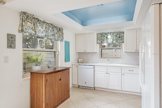 kitchen featuring a tray ceiling, a wealth of natural light, white appliances, and white cabinetry