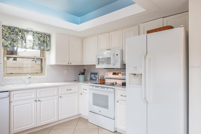 kitchen with a raised ceiling, sink, light tile patterned floors, white appliances, and white cabinets