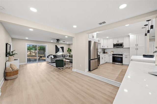 kitchen with stainless steel appliances, white cabinets, light stone counters, light wood-type flooring, and tasteful backsplash