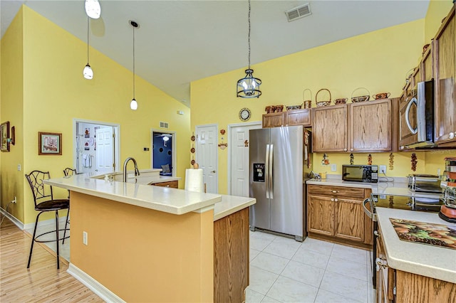 kitchen featuring decorative light fixtures, high vaulted ceiling, a kitchen island with sink, appliances with stainless steel finishes, and a kitchen breakfast bar