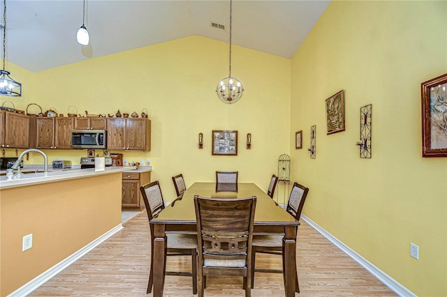 dining space with high vaulted ceiling, light hardwood / wood-style floors, a chandelier, and sink