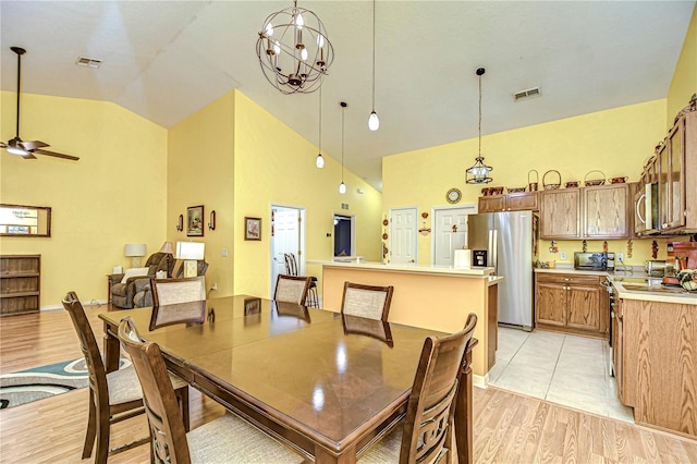 dining area featuring ceiling fan with notable chandelier, high vaulted ceiling, and light wood-type flooring