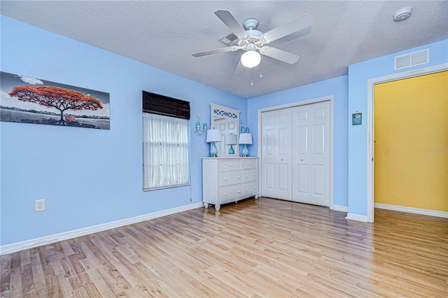 unfurnished bedroom with a textured ceiling, ceiling fan, light wood-type flooring, and a closet