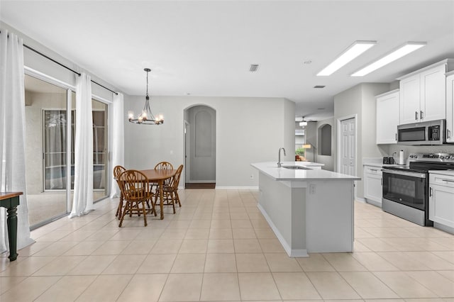 kitchen featuring appliances with stainless steel finishes, an island with sink, white cabinetry, and a notable chandelier