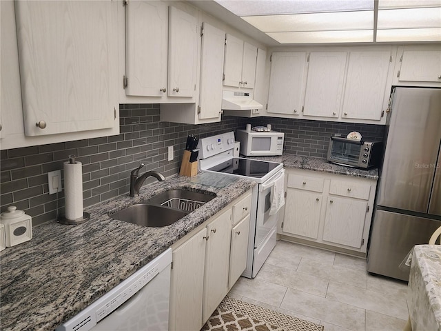 kitchen featuring backsplash, dark stone countertops, sink, white appliances, and light tile patterned floors