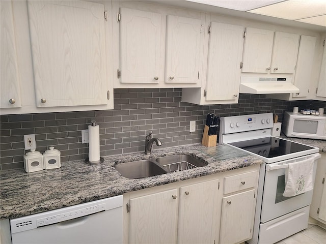 kitchen featuring backsplash, sink, white appliances, light tile patterned floors, and dark stone counters