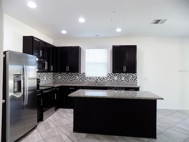 kitchen featuring appliances with stainless steel finishes, light stone counters, a kitchen island, and sink