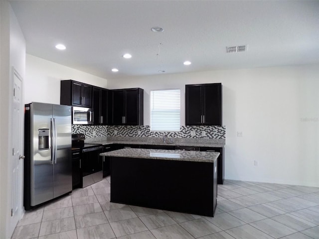 kitchen with backsplash, a kitchen island, light tile patterned flooring, light stone countertops, and stainless steel appliances