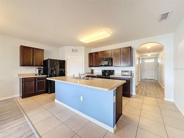 kitchen with a center island with sink, black appliances, light tile patterned floors, dark brown cabinetry, and sink