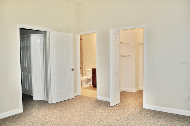 unfurnished bedroom featuring a spacious closet, light colored carpet, a closet, and ensuite bath