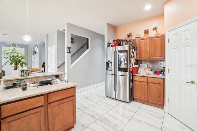 kitchen with stainless steel refrigerator with ice dispenser, light stone countertops, pendant lighting, and decorative backsplash