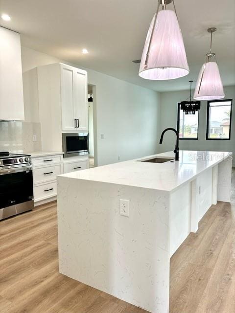 kitchen featuring stainless steel appliances, sink, white cabinetry, light hardwood / wood-style flooring, and hanging light fixtures